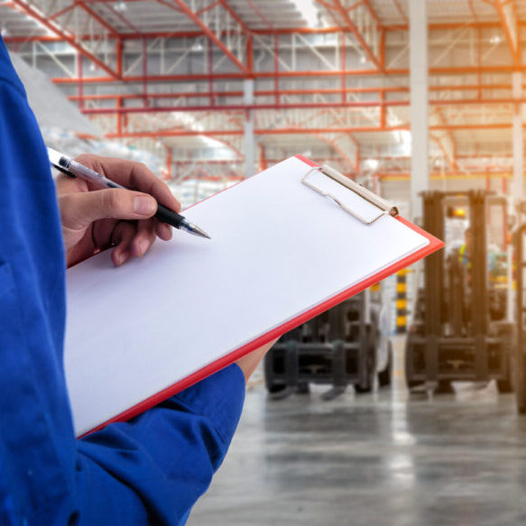 Worker checking document in front of the forklift at warehouse import export business.